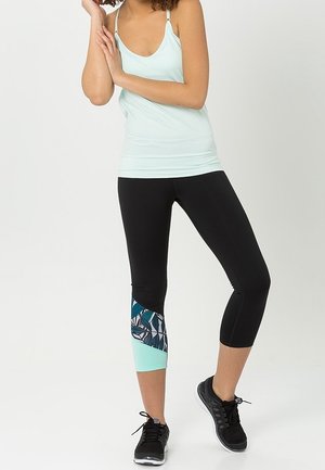 Un débardeur bleu clair associé à un legging capri noir avec un panneau en turquoise et bleu à motifs. Des chaussures de sport noires.