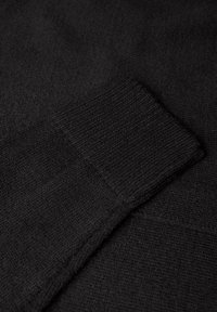 Svart stickad tröja med en strukturerad textil. Har ribbade ärmslut och en slät kropp, vilket visar subtila variationer i stickmönstren.