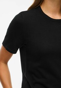 Juodas megztas trumpomis rankovėmis marškinėliai su apvalia iškirpte, turintys lygų paviršių ir subtilius siūlių akcentus ant pečių.