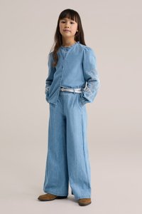 Heleroosa teksatop püstiste varrukatega ja keeruka valge tikandiga mansettidel, kombineeritud laiade säärega heleroosad teksapükste ja pruunide kingadega.