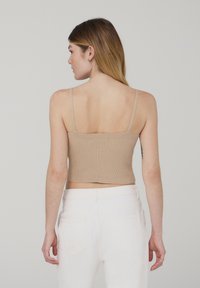 Top corto a coste beige con spalline sottili, design aderente e tessuto testurizzato, abbinato a pantaloni a vita alta di colore chiaro.