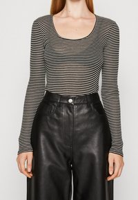 Černobílé proužkované tričko s dlouhým rukávem a výstřihem do tvaru kolečka, kombinované s černými koženými kalhotami s vysokým pasem a bočními kapsami.