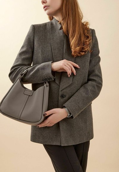 Blazer grigio in misto lana con un design strutturato, abbinato a una morbida borsa in pelle grigia, accentuato da un orologio argentato al polso.