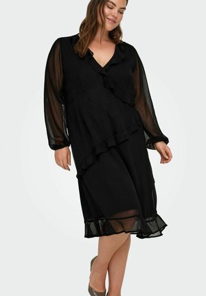 Juoda suknelė su volanų detalėmis, ilgomis permatomomis rankovėmis, V-kakleliu ir sluoksniuota sijona. Lygus audinys, kelių ilgio apdaila.