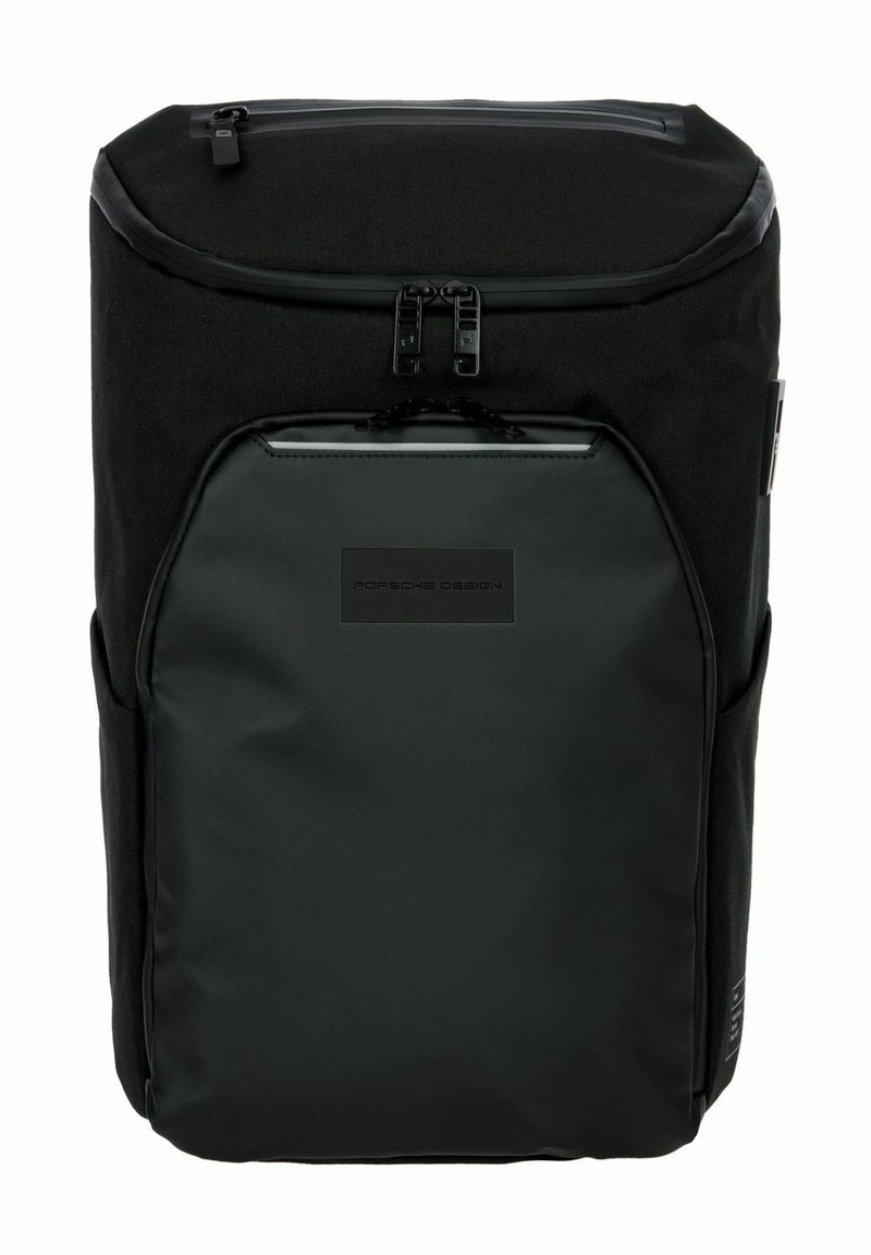 Mochila negra hecha de tela duradera; cuenta con una parte superior plana, cierres con cremallera, un bolsillo delantero y un parche con logo. Textura suave, diseño minimalista.