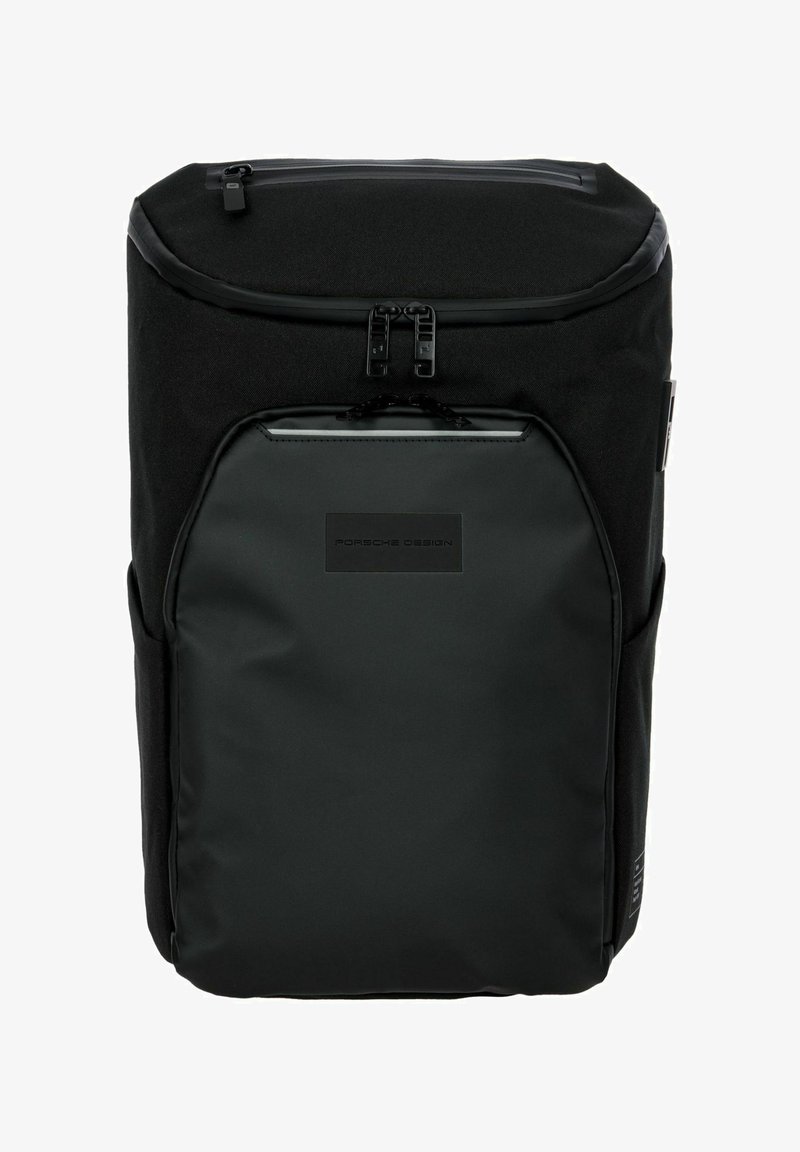 Mochila negra hecha de tela duradera; cuenta con una parte superior plana, cierres con cremallera, un bolsillo delantero y un parche con logo. Textura suave, diseño minimalista.