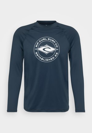 Rash guard de manga larga en color navy, hecho de un tejido suave. Presenta un logo circular blanco con "RIP CURL SURF CO ESTABLISHED 69" destacado.