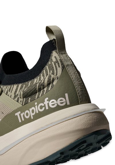 Gros plan sur le talon d'une chaussure de sport verte et beige avec une tige en maille texturée, un col noir, un onglet de tirage et la marque "Tropicfeel" sur le côté.