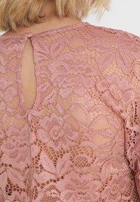 Lyserød blonde top med blomsterprint, semitransparent tekstur og en nøglehulrygdetalje, der er sikret med en knap.