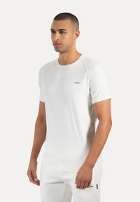 Weißes T-Shirt mit kurzen Ärmeln aus weichem Material, Rundhalsausschnitt und Raglanärmeln; mit kleinem Logo auf der Brust.