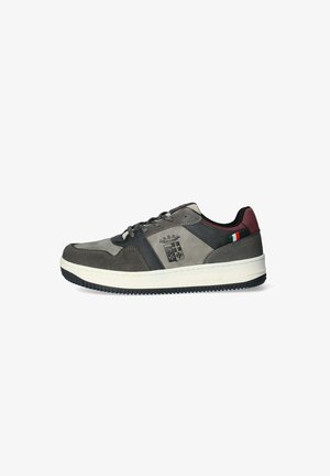 Sneaker realizzati in suede grigio con accenti scuri, suola in gomma e un logo. Presentano un dettaglio con una bandiera rossa e verde sul tallone.
