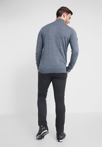 Suéter cinza de mangas longas com gola alta, combinado com calças cinza escuras e sapatilhas esportivas pretas, visto por trás contra um fundo branco.