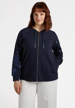 Marine blauwe rits-hoodie met paillettenversieringen op de mouwen. Voorzien van een capuchon, voorkruiszakken en een ontspannen pasvorm. Zachte stofstructuur.