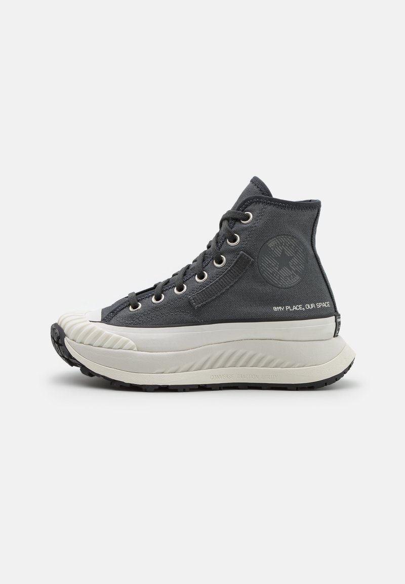 Baskets montantes en toile noire avec semelle blanche épaisse, bout texturé, fermeture à lacets à l'avant et écusson rond avec logo sur le côté.