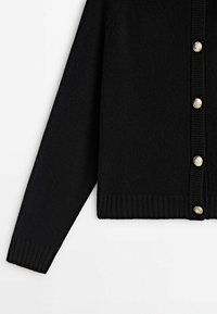 Cardigan noir en tricot avec manches longues et boutons décoratifs dorés le long du bord côtelé à l'avant.