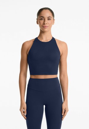 Top sportivo cropped blu navy con collo alto e design racerback, realizzato in un tessuto liscio e elastico. Abbinato a leggings a vita alta coordinati.