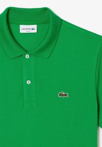 Green polo shirt made of textured cotton with a classic collar, two-button placket, and small embroidered crocodile logo on the chest.