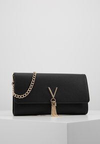 Pochette noire texturée avec une chaîne dorée, arborant un grand logo "V" doré et un détail à frange. Design minimaliste et épuré.