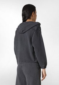 Sudadera corta con capucha en tela gris oscuro. Presenta puños elásticos, un cordón en el dobladillo y un corte relajado. Detalles de costura simples.