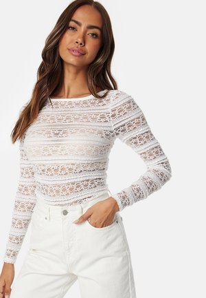 Vit spetsblus med långa ärmar som har ett horisontellt randigt mönster med intrikata designer, matchad med högmidjade vita denimjeans.