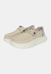 Chaussures en toile beige avec un embout arrondi, semelle en caoutchouc blanche et intérieur à motifs contrastés ; elles présentent un détail de lacet avec des accents bleu foncé.