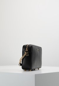 Czarna, prostokątna torebka wykonana z fakturowanego materiału, z złotym łańcuszkowym paskiem, zamkiem błyskawicznym i małymi metalowymi nóżkami.