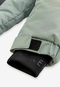 Mätničká zelená izolovaná obal s velcro pásikom, čierny interiér s textom. Hladký povrch, prešitý dizajn a praktické pre teplo.