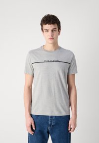 Gray cotton t-shirt with a round neckline, featuring a black printed "Calvin Klein" logo across the chest on a horizontal line.