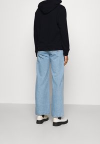 Granatowa bluza z kapturem, w zestawieniu z jasnoniebieskimi spodniami o szerokich nogawkach i czarnymi botkami za kostkę z białym akcentem oraz pętlą do zakładania.