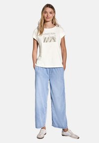 Hvid bomulds T-shirt med "INFINITE BLISS" grafik, parret med lyseblå brede bukser og hvide sneakers. Modellen står med hænderne i lommerne.