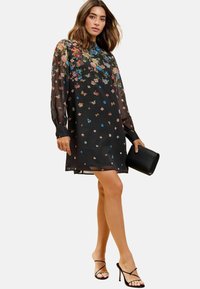 Rochie neagră cu flori, cu manșete lungi din material transparent. Prezintă flori și fluturi brodați colorat. Asortată cu o poșetă neagră și tocuri.
