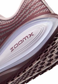 Close-up af en pink og lilla atletiksko med sål, der har "ZoomX" stødabsorbering og tekstureret mønster for bedre greb.