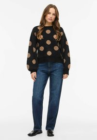 Must merinovillane pusa suurte beežide täppidega, õhupallivarrukad ja soonikkoes mansetid. Kombineeritud sirge säärega siniste teksade ja mustade kingadega.