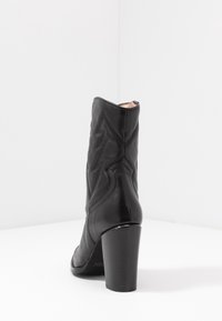 Černá kožená kotníková bota s blokovým podpatkem, s prošíváním a špičatým designem na zadní straně. Hladký povrch, bez ozdob.