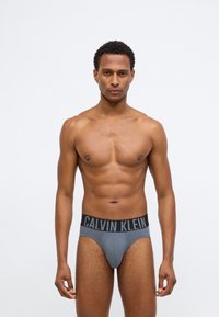 Ανδρικά γκρι βαμβακερά σλιπ με μαύρη ελαστική ζώνη που φέρει το λογότυπο "Calvin Klein" σε έντονη γραφή. Λείος υφασμάτινος τύπος, σχεδίαση που εφαρμόζει.