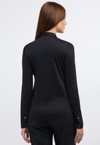 Schwarzes Langarmshirt mit weicher, glatter Textur, klassischem Kragen und Knopf-Details an den Manschetten. Taillierte Passform.