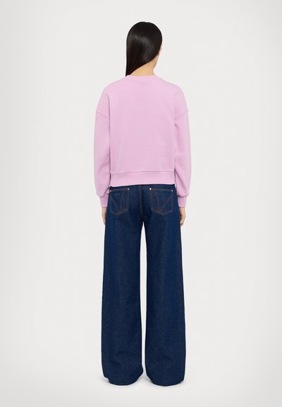 Vaaleanpunainen lyhyt huppari, jossa on pitkät hihat ja ribbireunat, yhdistettynä leveisiin tummansinisistä farkuista, joissa on eriväriset saumat ja taskut.