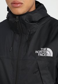Černá kapucová bunda z voděodolného materiálu s předním zipem, nastavitelnými šňůrkami a bílým logem na hrudi.