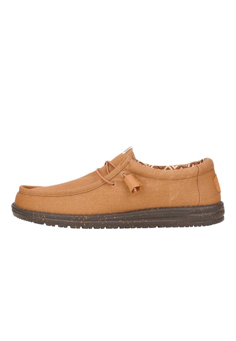 Zapatillas de lona color beige sin cordones, con punta redonda, detalle de cordones y plantilla estampada. La suela de goma presenta un diseño salpicado para ofrecer tracción.