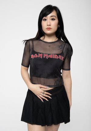 Black mesh shirt with "IRON MAIDEN" in red letters, paired with a black pleated skirt. Short sleeves and sheer fabric with subtle pattern.