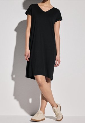 Czarna sukienka z dekoltem w serek, krótkimi rękawami, miękkiego materiału, luźny krój i zaokrąglony dół. W zestawieniu z jasnymi, teksturowanymi sneakersami.