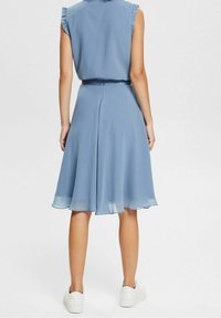 Vaalea sininen, hihaton mekko, jossa on röyhelökoristelut olkapäillä, valuva hame ja muotoiltu vyötärö. Yhdistetty valkoisiin lenkkitossuihin rentoa ilmettä varten.