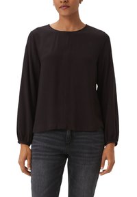 Black long-sleeve blouse with a round neckline, featuring a front seam detail and slightly gathered cuffs, paired with dark jeans.