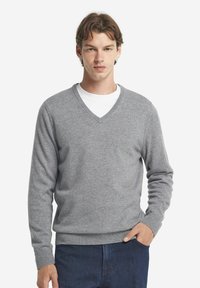 Grauer V-Ausschnitt Pullover aus weichem Strickmaterial, mit langen Ärmeln und gerippten Bündchen. Über einem weißen T-Shirt getragen, mit lockerem Schnitt.
