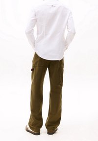 Camicia bianca a maniche lunghe con orlo arrotondato, abbinata a pantaloni cargo verdi oliva con più tasche e un'etichetta con logo sulla vita.