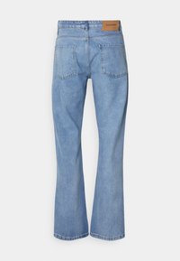 Jeans in denim azzurro chiaro con una vestibilità rilassata, gambe a zampa d'elefante e due tasche posteriori. Presentano una patch in pelle marrone in vita.