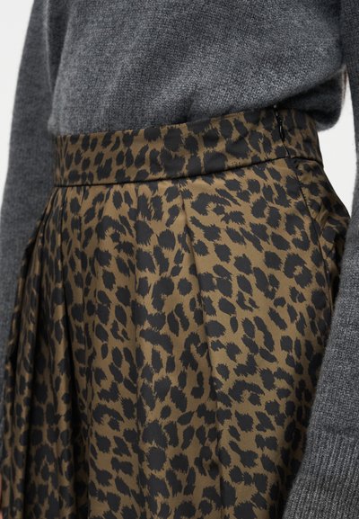 Pás a boky osoby nosiacej hnedú a čiernu sukňu s leopardím vzorom a sivý pletený sveter.