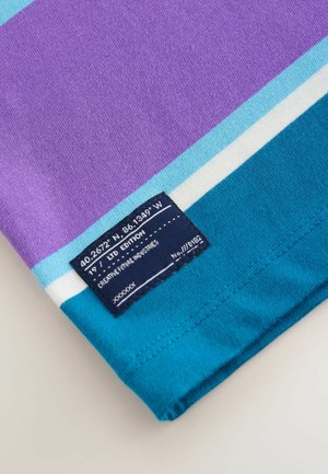 Trumpas rankovėmis marškinėliai su violetinėmis, turkio ir baltomis juostelėmis. Apima tamsiai mėlyną etiketę su koordinatėmis ir tekstu "LTD EDITION".