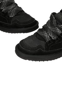 Zwarte sneakers hebben een mesh bovenwerk met suède accenten, textuurveters in zwart en grijs, en een rubberen zool met een onderscheidend profiel.