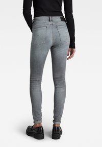Jeans gris de corte slim, de tiro alto, con una textura descolorida, cinco bolsillos y costuras en contraste. Combinados con zapatos de plataforma negros.